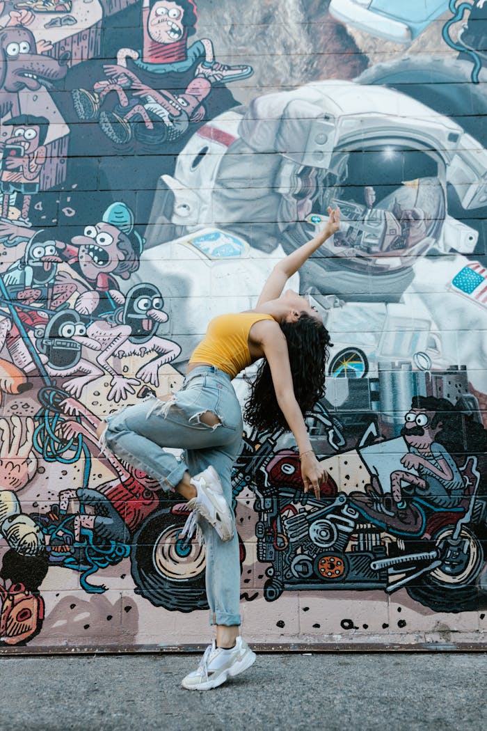 Woman performing contemporary dance against a colorful graffiti art mural, showcasing urban street style.